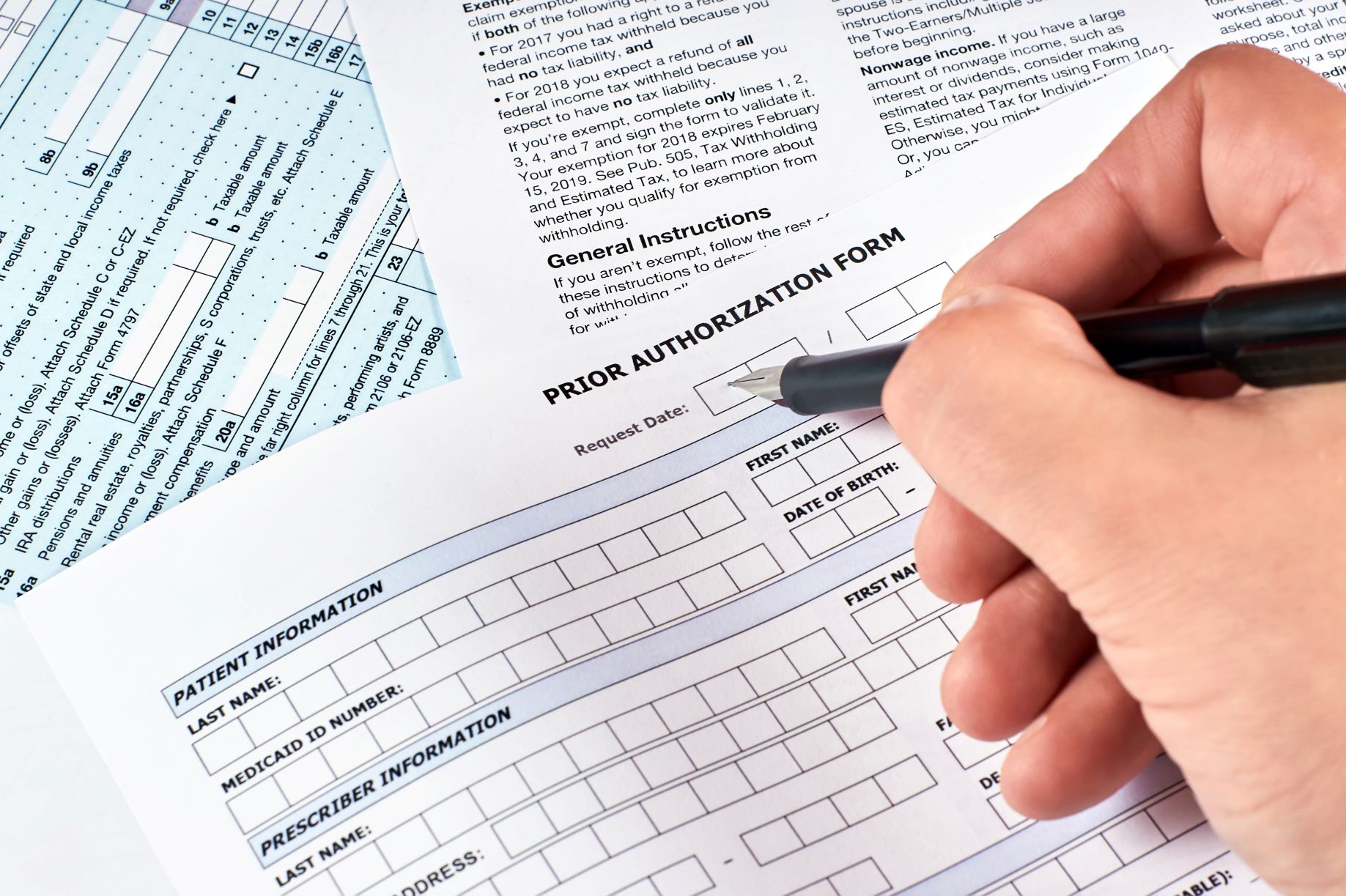 Closeup of someone's hand filling out a printed prior authorization form.